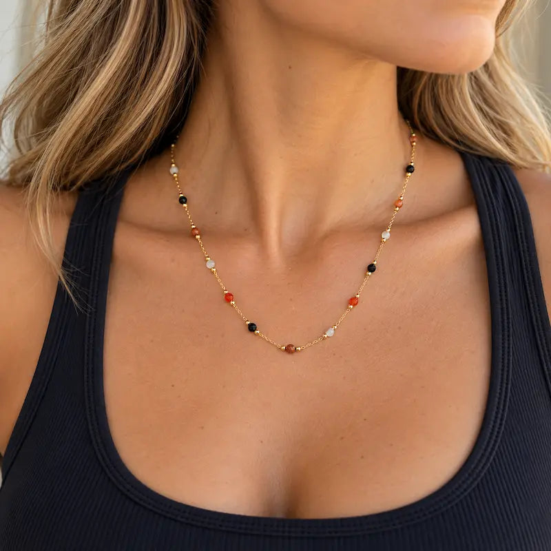 Woman wearing the Autumn Confetti 18K gold beaded necklace with a black athleisure top, featuring delicate colorful stones on an 18-inch gold chain.