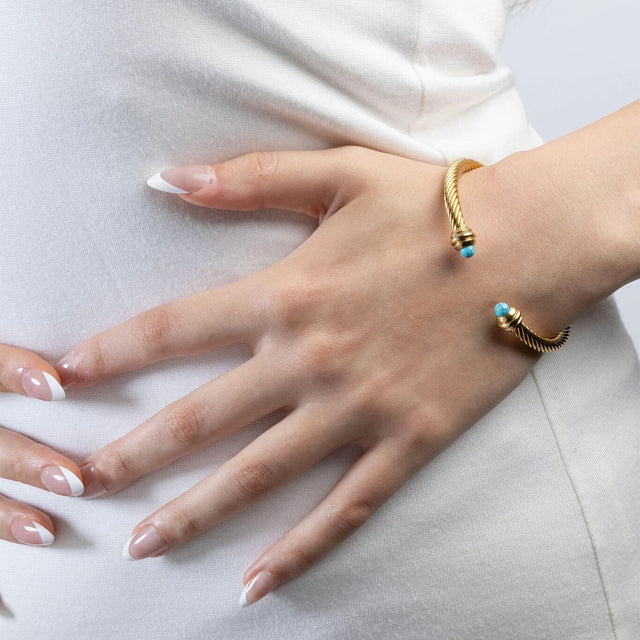 Hand wearing a gold bracelet with turquoise stones hand on hip
