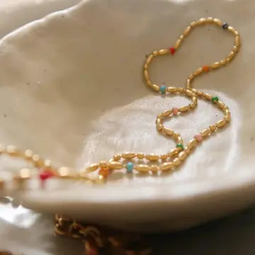 18K gold sun charm necklace with colorful beads shown in a dish