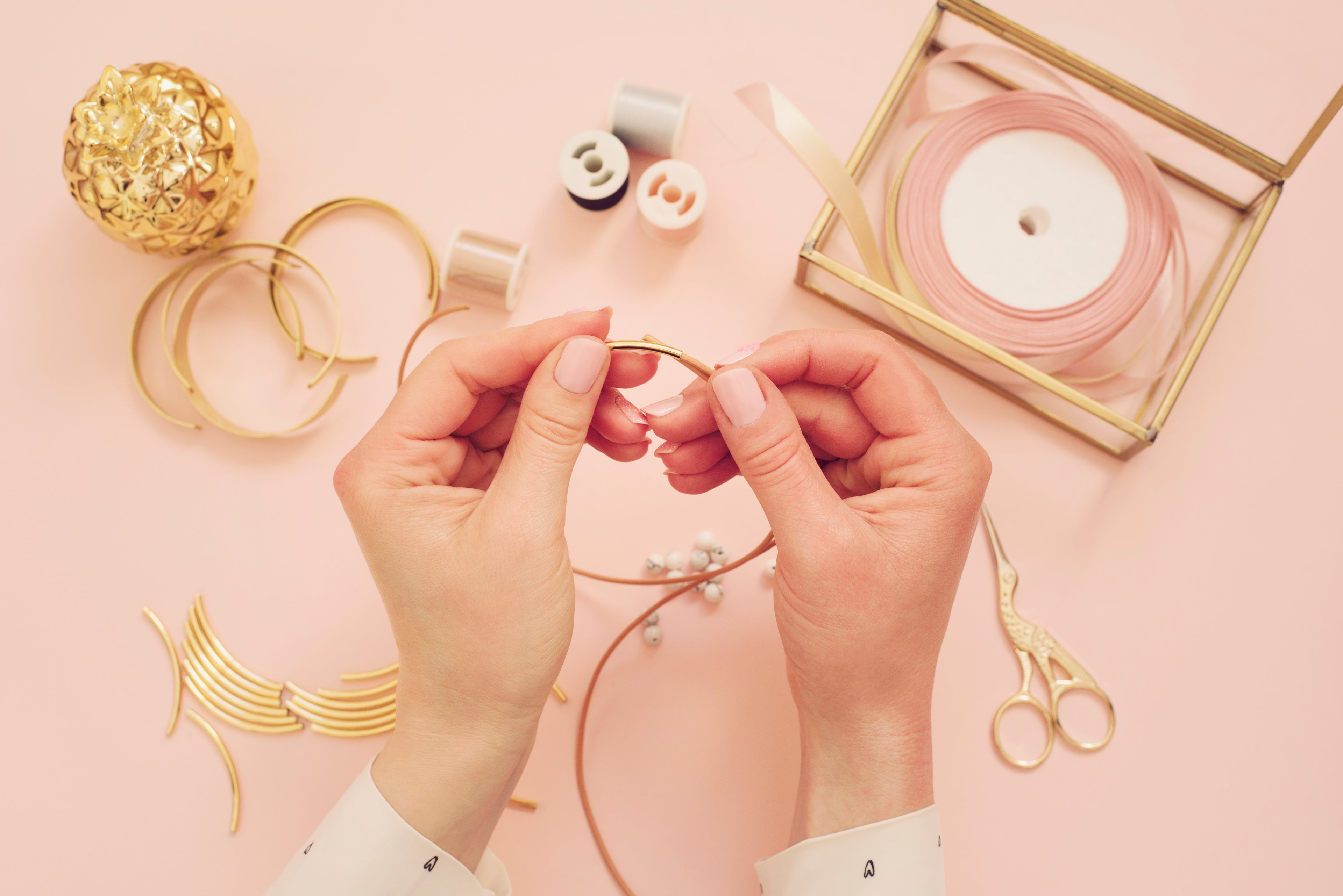 Hands working with jewelry on a pink background